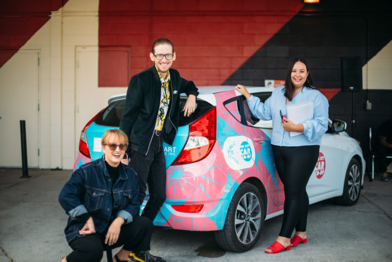 synonym team standing near Peg City Car Co-op Image Wrapped vehicle