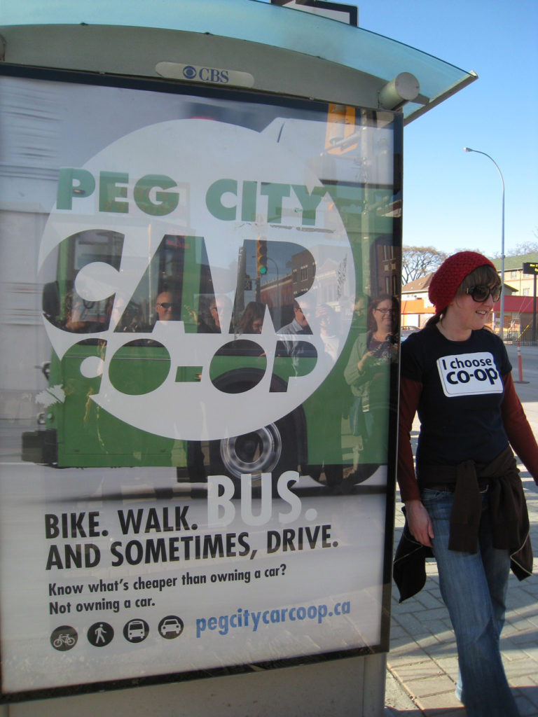 co-op member stands beside Peg City Car Co-op Bus shelter Ad